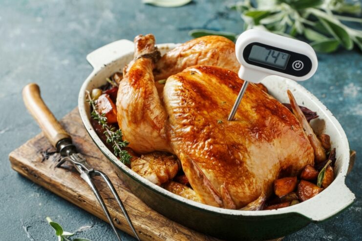 Golden brown roasted chicken with a digital thermometer inserted into the thickest part of the breast.