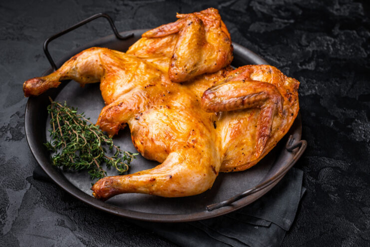 Spatchcocked chicken with crispy golden skin resting on a metal baking sheet surrounded by sprigs of fresh thyme.