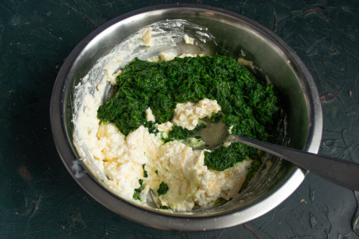Mixing spinach with the cheese base Folding cooled cooked spinach into the cheese and egg mixture