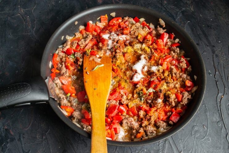 Seasoning the meat sauce Spices, paprika, and dried herbs sprinkled over the simmering meat sauce.