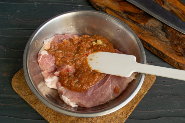 Marinating the Pork Pork coated in a thick marinade inside a metal bowl.