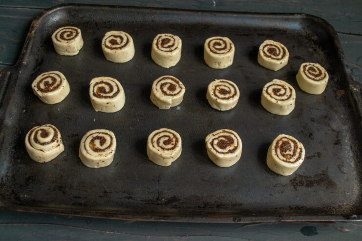 Arranging on a baking sheet Raw poppy seed pinwheels spaced out on a baking sheet.