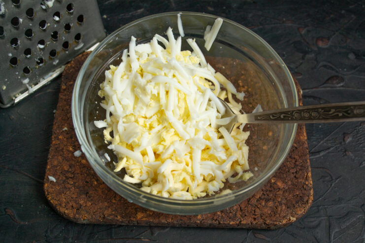 Grated hard-boiled eggs and processed cheese in a mixing bowl