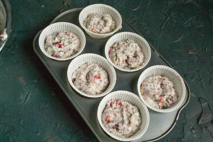 Batter evenly divided into paper liners inside a metal muffin tin.