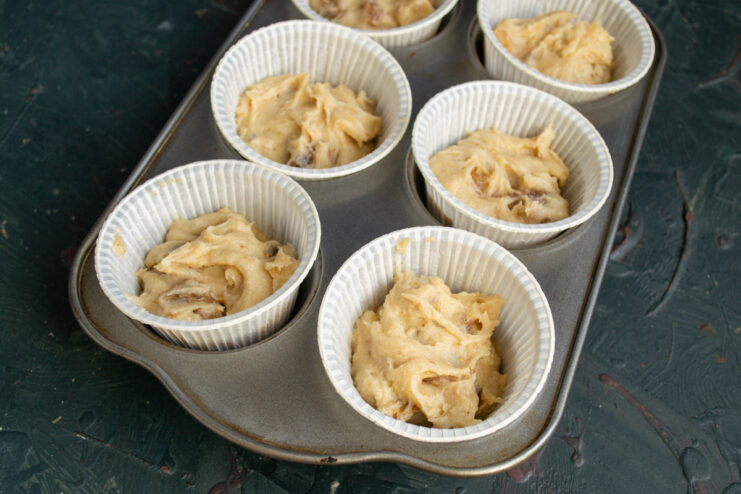 Portioning the batter Fig muffin batter evenly distributed into paper cups inside a metal baking tin.