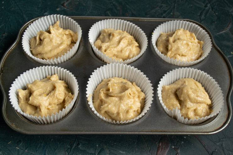 Filling The Liners Scooping muffin batter into paper liners inside a metal baking tin