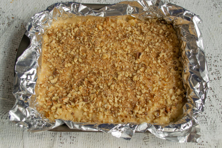 Sprinkling walnuts over the batter Cake batter in a rectangular baking dish sprinkled with chopped walnuts