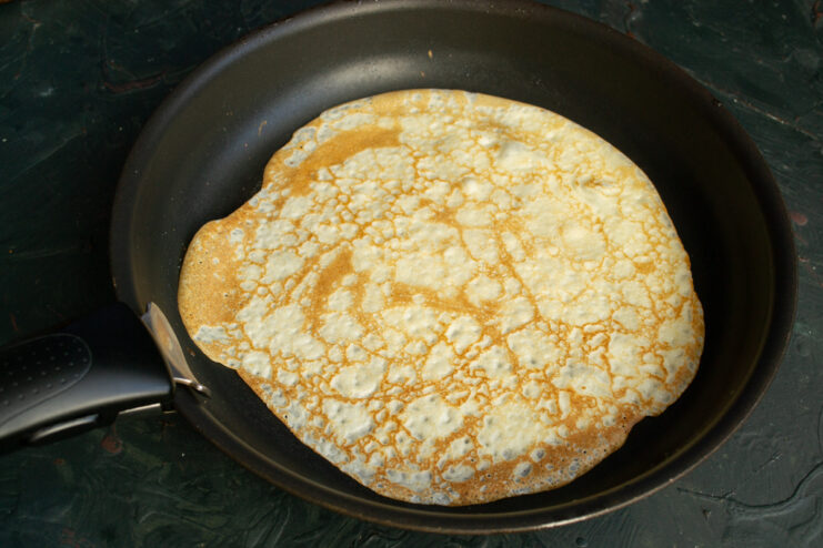 A thin crepe frying in a skillet until golden brown.