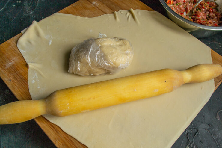 Rolling the dough to a thin sheet Thinly rolled sheet of dough on a wooden board with a rolling pin
