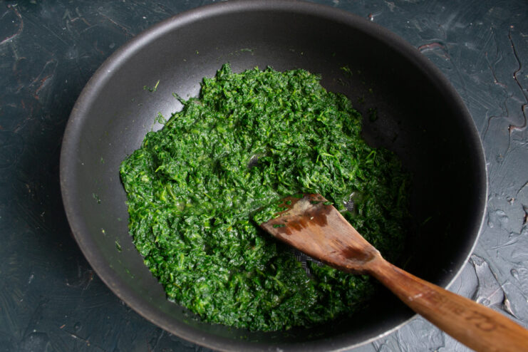 Evaporating moisture from the spinach Cooking green spinach in a skillet to evaporate excess moisture