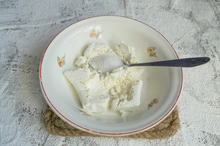 Preparing the cheese base Mixing farmer's cheese with sugar in a glass bowl