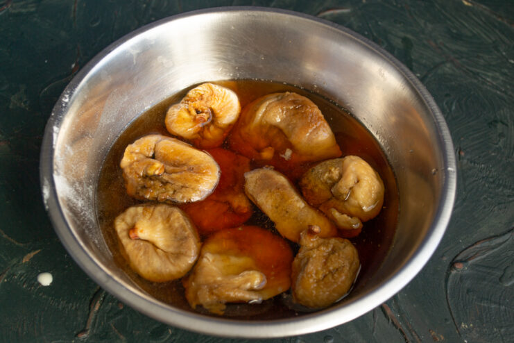 Dried figs soaking in a metal bowl filled with water.