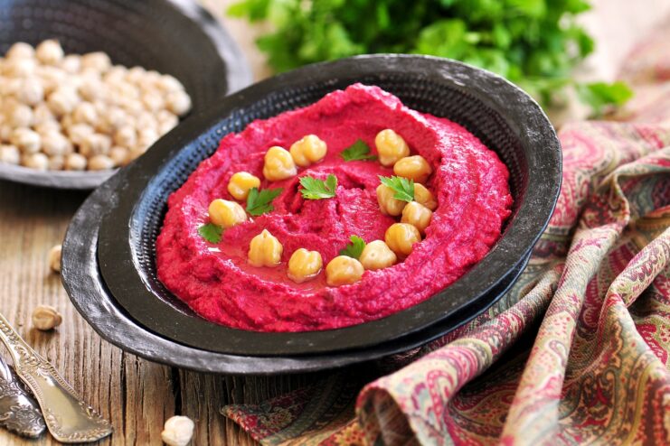 Modern Vibrant Beetroot Hummus Bright beetroot hummus served in a black bowl garnished with whole chickpeas and fresh herbs.
