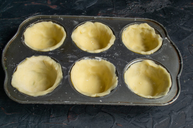 Raw shortbread dough circles pressed into the cavities of a metal muffin tin.