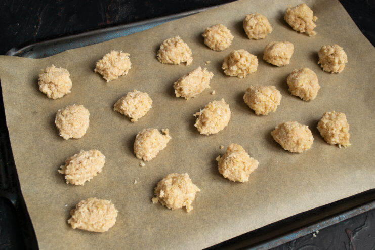 Portions of sticky cookie dough on a parchment-lined baking sheet