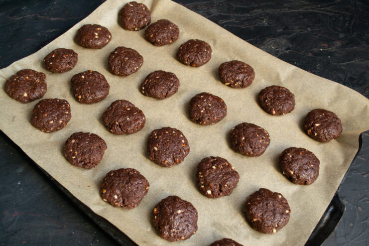 Shaping the Cookies Raw chocolate cookie dough balls flattened on a parchment-lined baking sheet