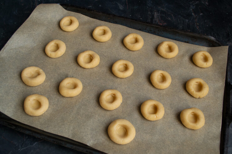 Creating thumbprints Cookie dough balls with indented centers on a parchment-lined baking sheet.