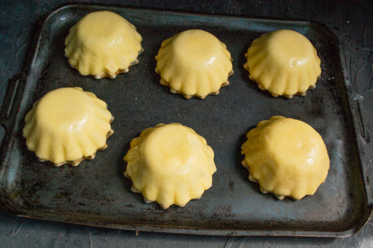 Preparing for the Oven Raw dough bases molded over muffin tins on a baking sheet