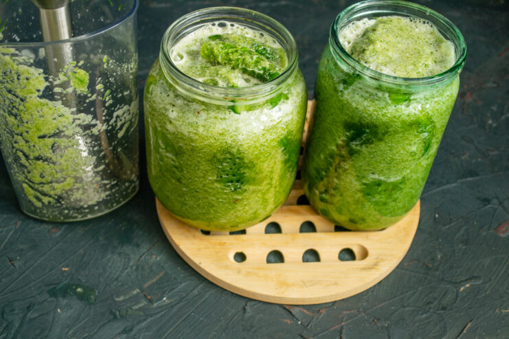 Filling jars with green brine Pouring vibrant green brine into glass jars over tightly packed cucumbers