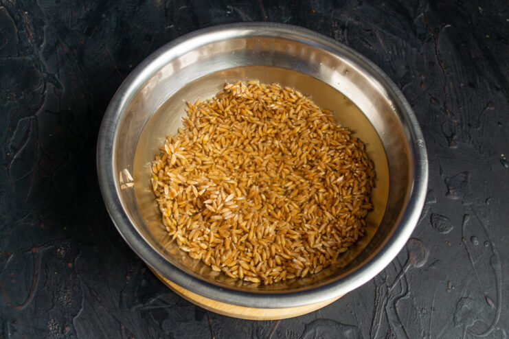Soaking the spelt grains Raw spelt grains soaking in cold water inside a metal bowl.