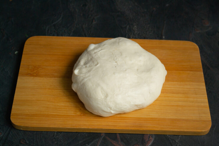 Working with the soft dough Kneaded yeast dough for smazhenka on a wooden cutting board.