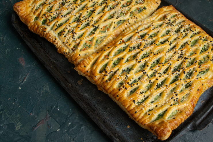 Baking the tart to a golden brown Golden baked spinach and ricotta puff pastry tarts on a tray