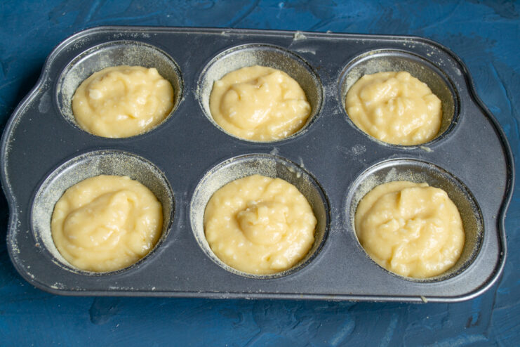 Portioning the batter Muffin tin cavities partially filled with batter.