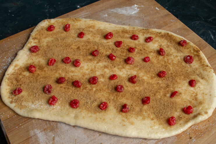 Adding candied cherries Candied cherries scattered over cinnamon layered dough