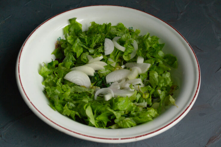 Adding Lettuce and Onion Green lettuce and sliced onions in a mixing bowl