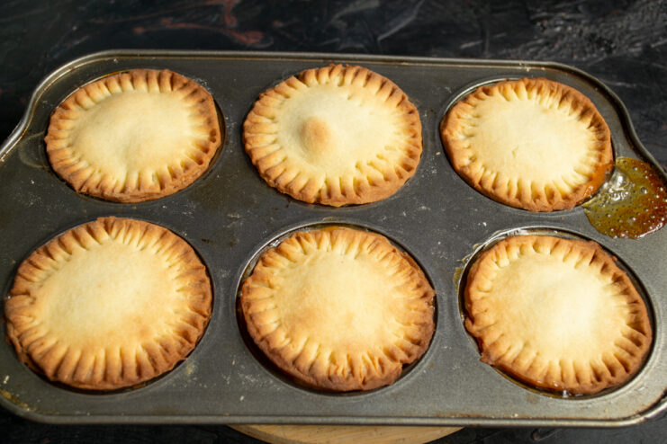 Golden brown baked tartlets sitting inside a metal muffin tin.