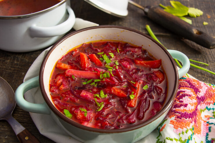 Appetizing red borscht served in a bowl topped with sour cream and fresh herbs.