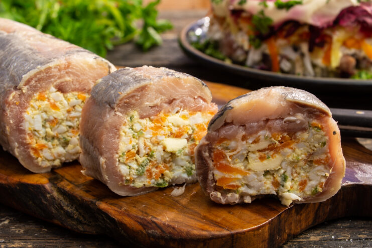 Appetizing herring roll with butter and vegetables sliced on a wooden board.