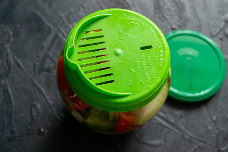 Warming the vegetables with boiling water Glass jar of vegetables capped with a green straining lid for draining