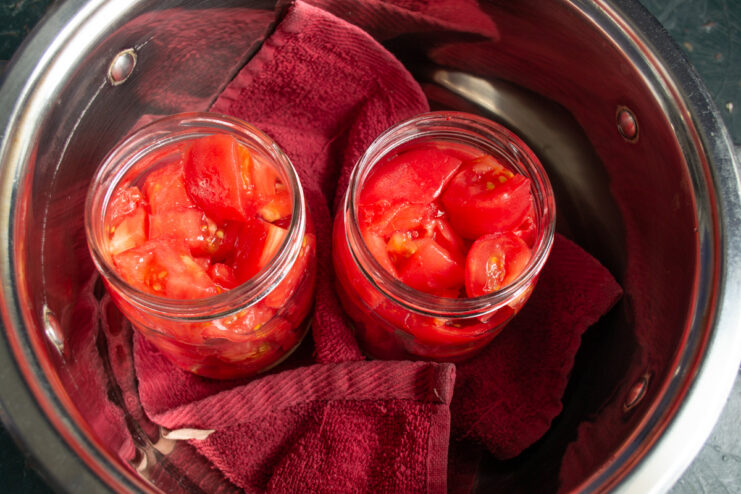 Protecting jars with a cloth napkin for sterilization Glass jars with tomatoes sitting on a cloth napkin inside a large deep pot