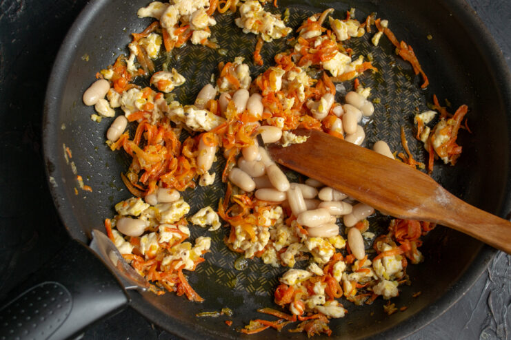 Mixing beans into the filling Stirring white beans with cooked chicken and vegetables in a skillet