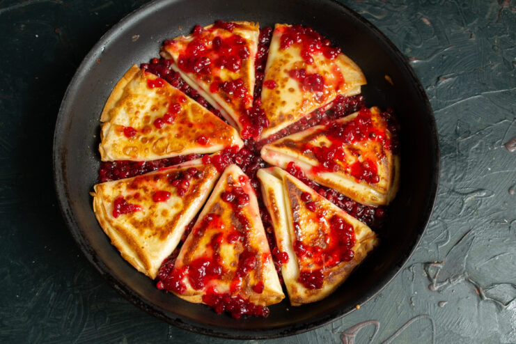 Golden crepes in a skillet covered in rich lingonberry jam