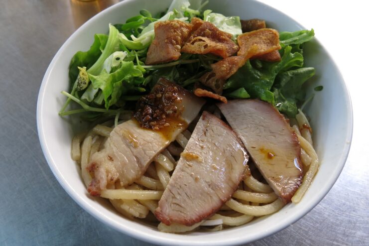 Regional cao lau noodle dish from Hoi An Bowl of cao lau thick noodles topped with roasted pork and fresh greens.