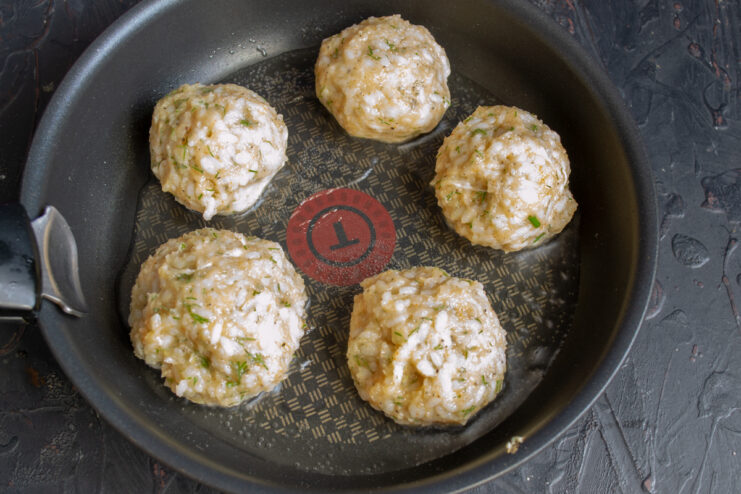 Browning The Meatballs Large round chicken meatballs frying in a skillet with oil.