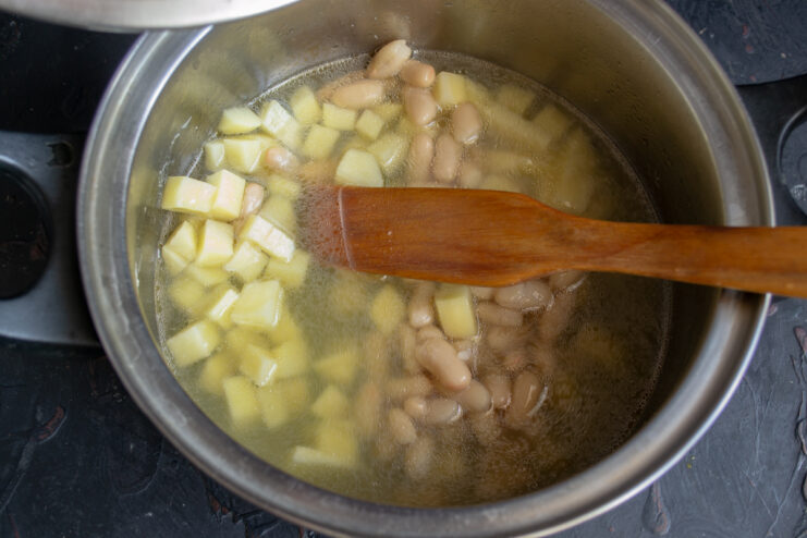 Pouring broth over the vegetables Pouring hot strained chicken broth over potatoes and beans