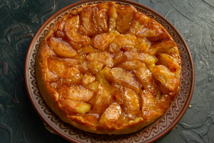 Whole upside-down apple tart with shiny caramel on a brown serving dish.