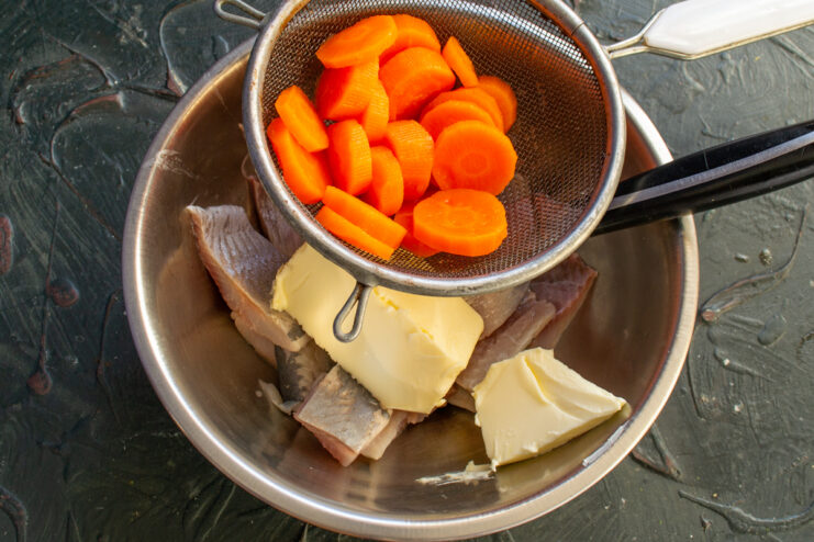 Mixing ingredients Adding blanched carrots through a sieve to fish and butter