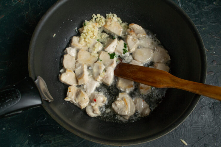 Adding minced garlic to the seared chicken in the pan