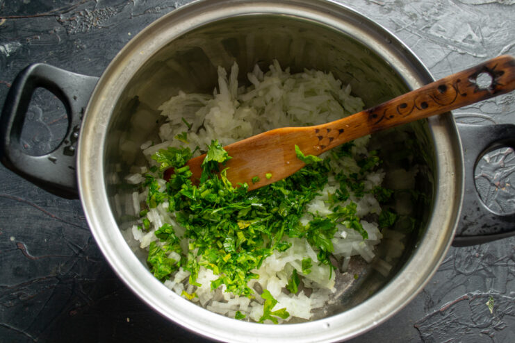 Adding herbs for the soup Stirring finely chopped fresh herbs into the sautéed onions