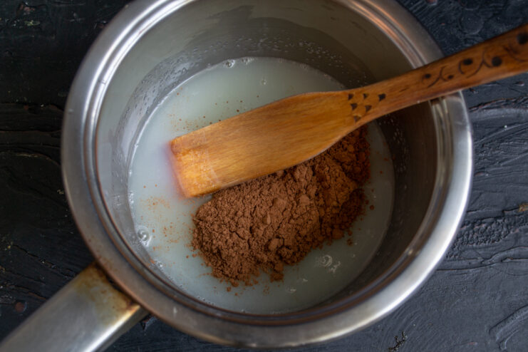 Adding cocoa to the syrup Whisking dark cocoa powder into the creamy syrup inside a saucepan