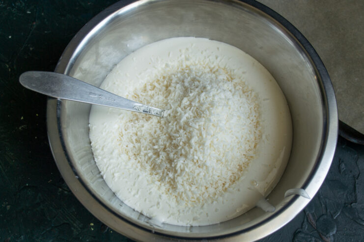 Adding the coconut flakes. Folding desiccated coconut into the beaten egg mixture in a metal bowl.