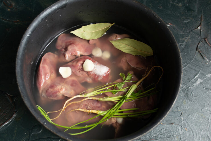 Adding aromatics to the broth Adding parsley roots, garlic slices, and bay leaves to the saucepan with chicken liver.