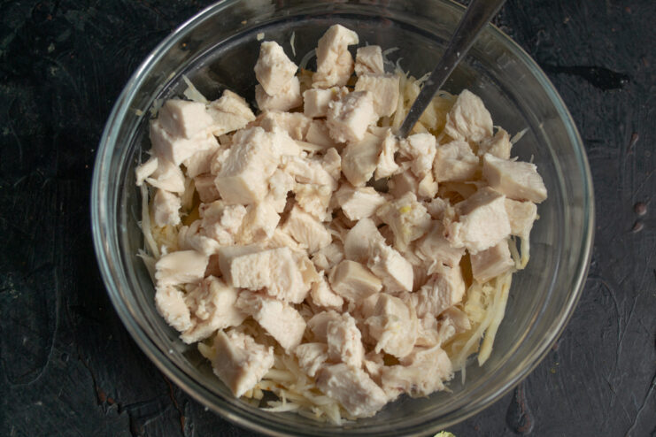 Combining celeriac and chicken Adding diced cooked chicken to blanched celeriac in a bowl