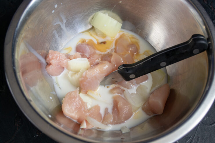 Adding Binders To The Mixture Adding an egg and heavy cream to chopped chicken and onions in a bowl.