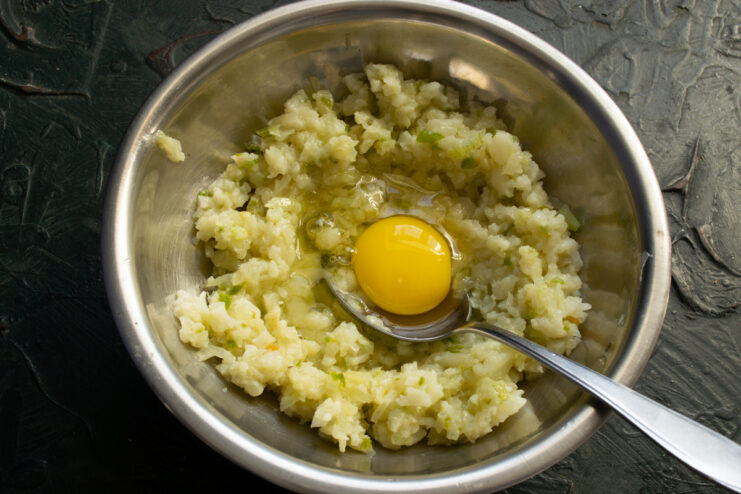 Adding The Binder Adding a raw chicken egg into the minced cauliflower mixture