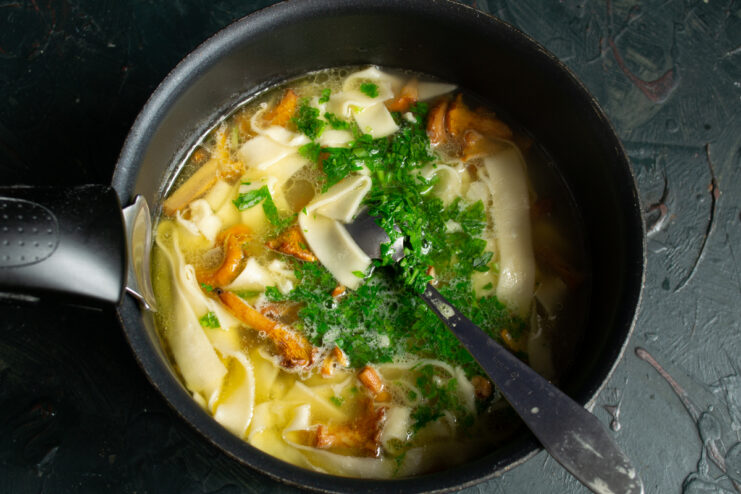 Final cooking stage Adding homemade noodles and chopped parsley to the pot of soup